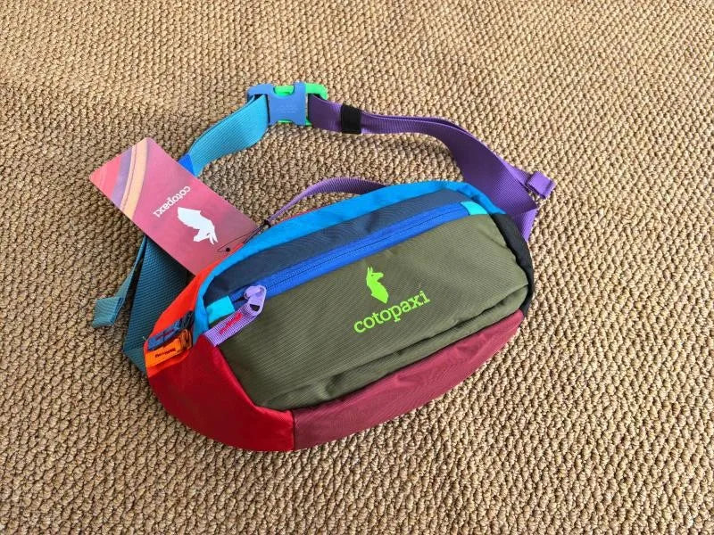 A color block waterproof nylon fanny pack with multiple colored straps and a green main compartment resting on a brown textur