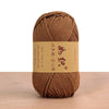 A ball of brown cotton blend crochet yarn with a tan label resting on a wooden surface.