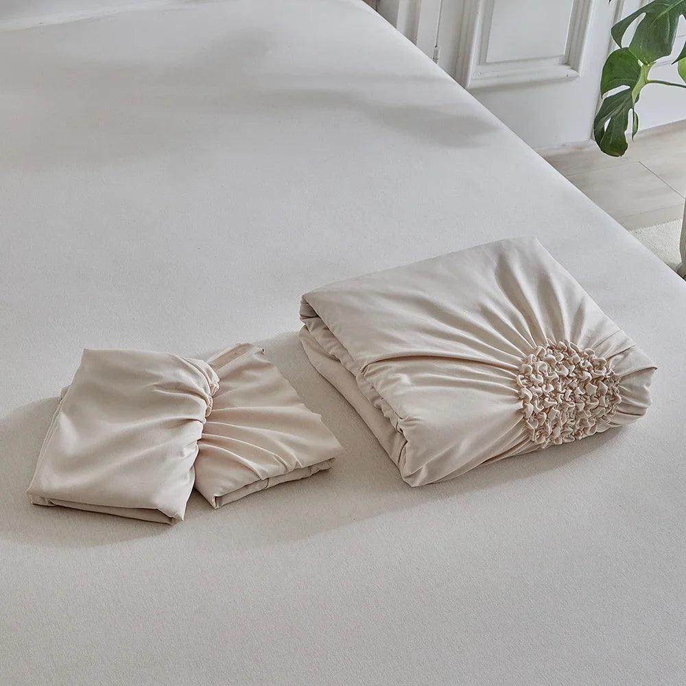 A set of three-dimensional pleated floral duvet covers in a soft beige color displayed on a white bed.