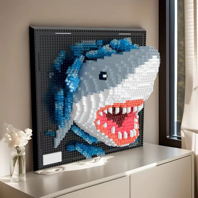 A framed wall art piece depicting a shark face made from blue and white mosaic building blocks.