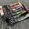 A collection of black leather keychains with various text designs and clasps laid on a textured surface.