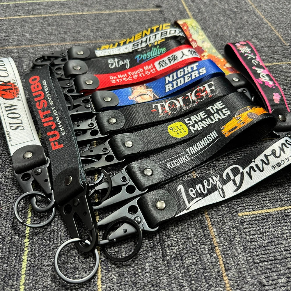 A collection of black leather keychains with various text designs and clasps laid on a textured surface.