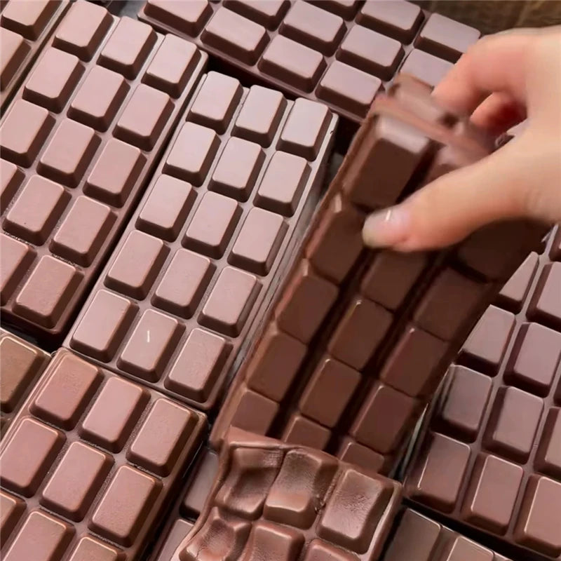 A hand is pressing a realistic brown chocolate bar fidget toy with a grid pattern.