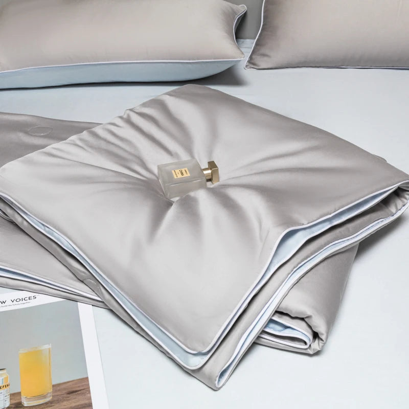 A folded light gray ice silk quilt with a gold zipper is displayed on a white surface.