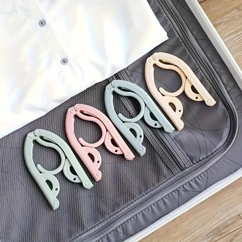 A set of ten light colored foldable travel clothes hangers with anti-slip grips displayed on a gray fabric surface.