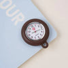 A brown silicone pocket watch with a clear face and a pink floral detail is shown resting on a light blue notebook.