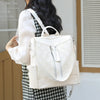 A woman is carrying a cream-colored anti-theft leather backpack with silver zippers and a white shirt.
