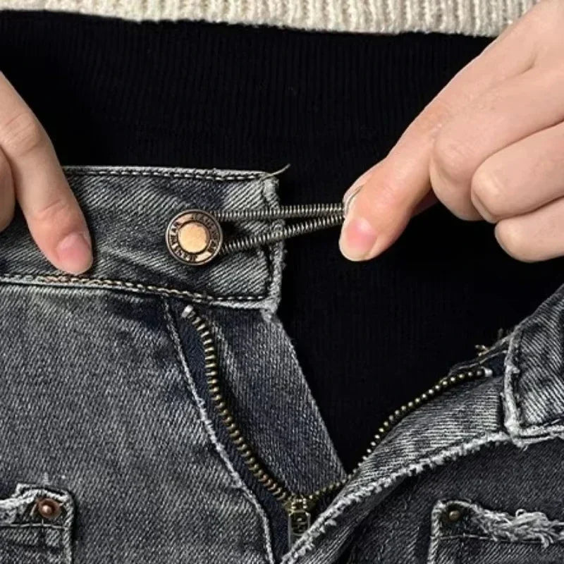 A hand is adjusting an adjustable metal button on the waistband of dark denim jeans.
