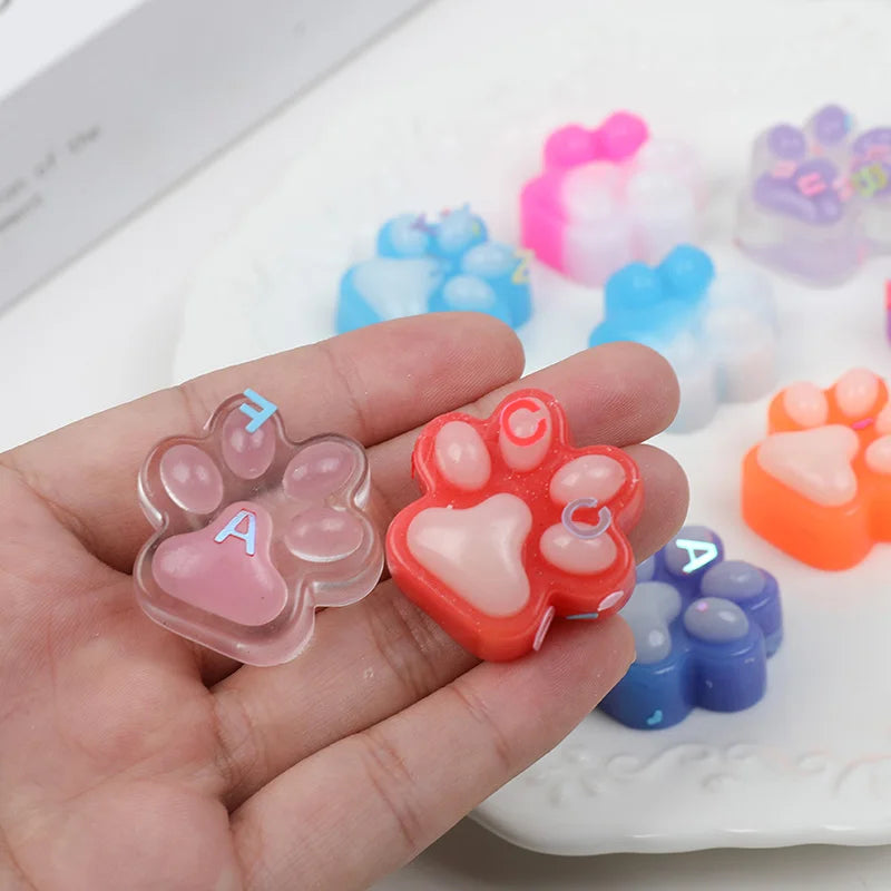 A hand holds various squishy cat paw fidget toys in pink, orange, and blue colors.