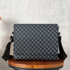 A dark gray patterned crossbody bag resting on a wooden stool against a light gray background.