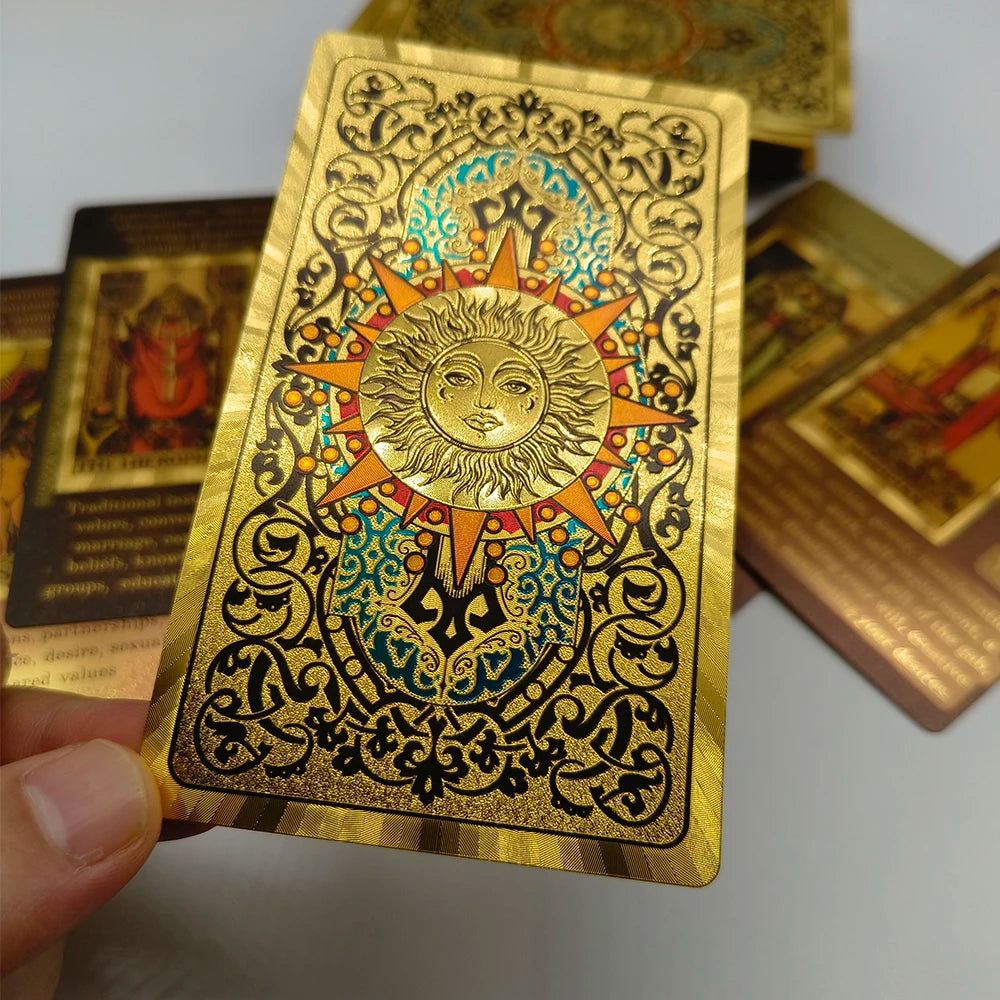 A gold foil tarot card featuring a sun design and intricate decorative borders, held by a hand.