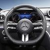 Close-up view of a black steering wheel with carbon fiber texture covers and digital instrument cluster in a Mercedes-Benz in