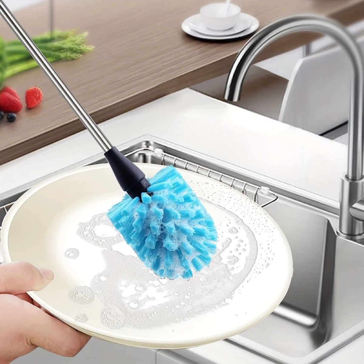 A hand is using a blue sponge brush on a white plate under a kitchen faucet for cleaning.