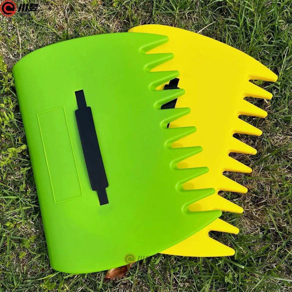 A pair of bright green and yellow ergonomic leaf grabber rake tools lying on green grass.