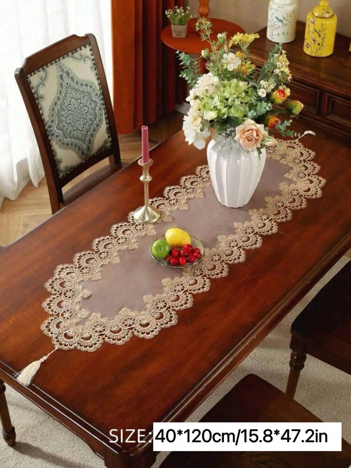 A brown wooden table is decorated with a sheer lace runner and fruit, set in a traditional interior.