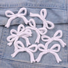 White embroidered iron-on bow patches scattered on a denim fabric surface