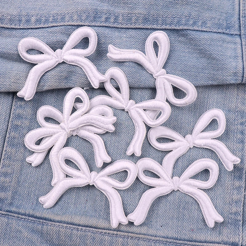 White embroidered iron-on bow patches scattered on a denim fabric surface