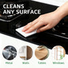 A hand uses a white magic eraser sponge to clean a black stovetop surface.