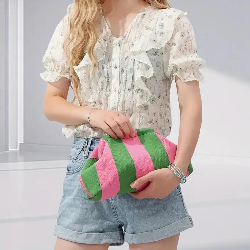 Une femme modèle un sac à main en crochet rayé rose et vert avec une blouse florale blanche et un short en denim.