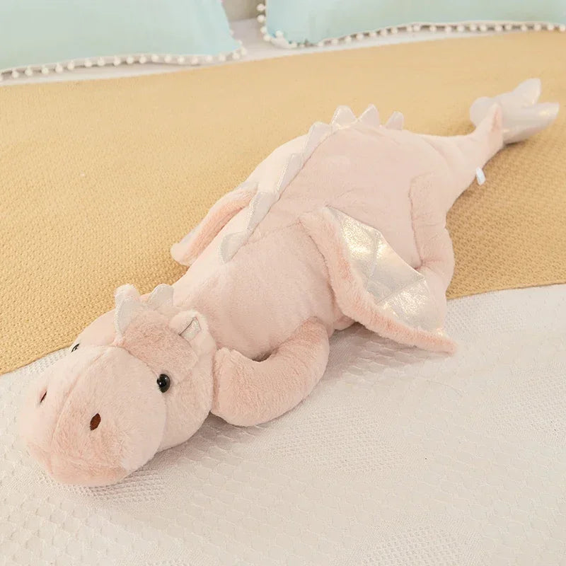 A soft pink dragon plush pillow is lying on a white surface.