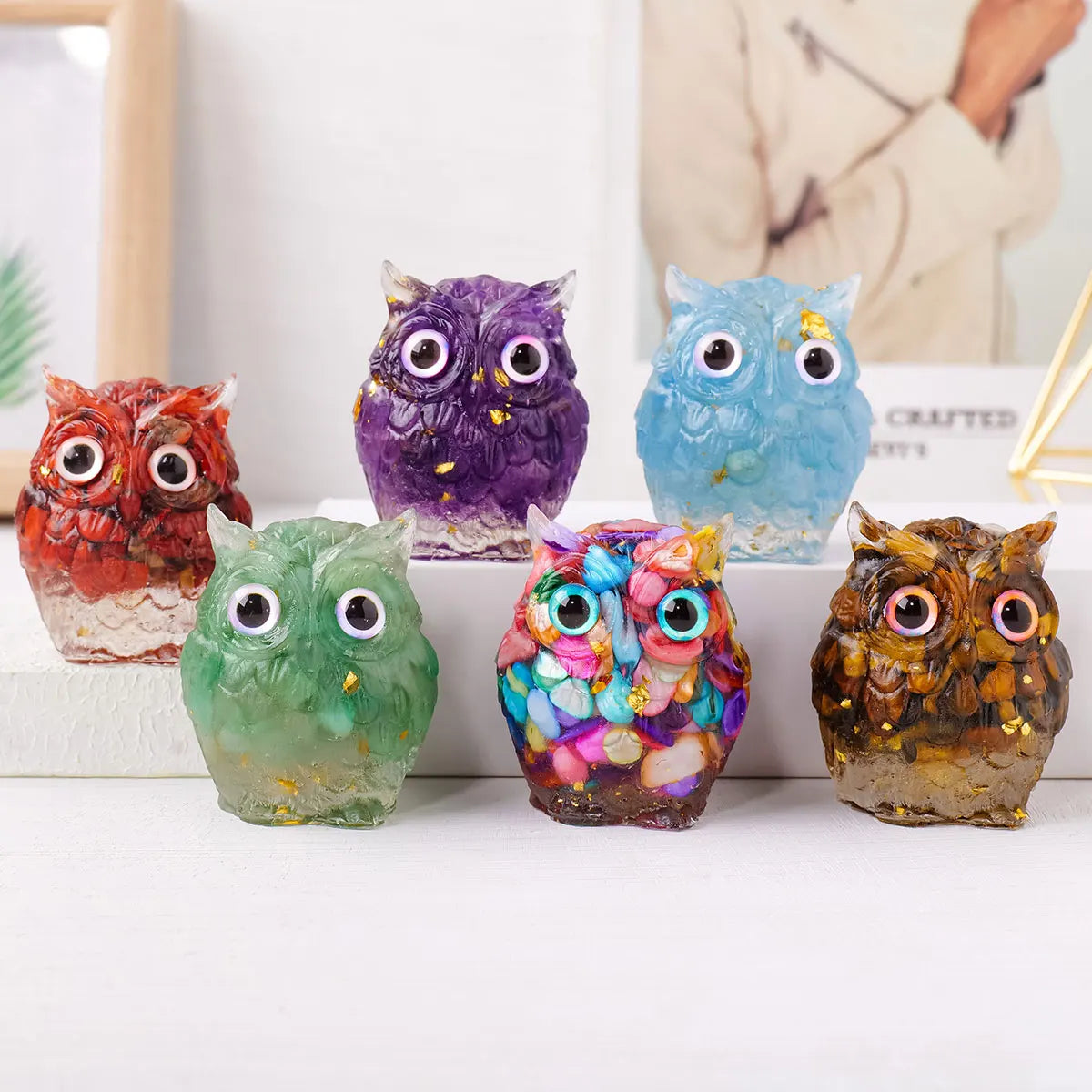 A collection of handcrafted crystal owl figurines in various colors and finishes displayed on a white surface.