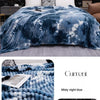 A blue tie-dye flannel fleece throw blanket draped over a bed, featuring a mottled pattern.