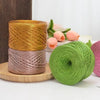Spools of metallic flat ribbon yarn in gold and rose tones resting on a wooden surface.