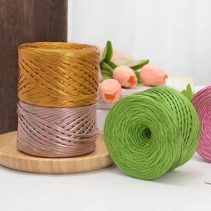 Spools of metallic flat ribbon yarn in gold and rose tones resting on a wooden surface.