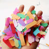 A hand holds a pile of colorful confetti paper shreds in various shades of pink, green, orange, and purple.