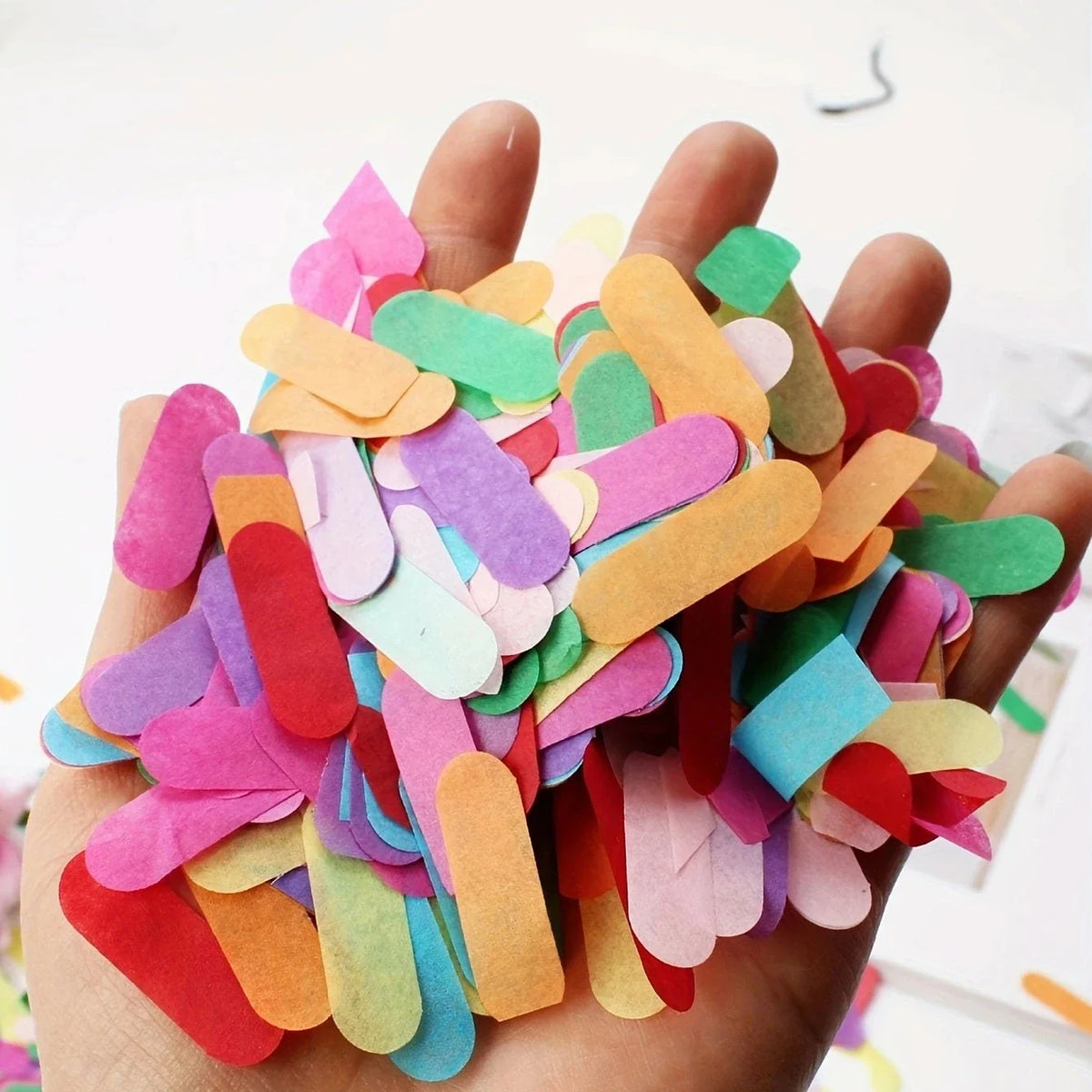 A hand holds a pile of colorful confetti paper shreds in various shades of pink, green, orange, and purple.