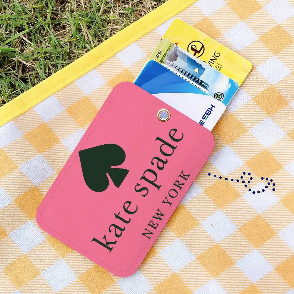 A pink card holder with a spade design rests on a yellow checkered cloth next to a stack of credit cards.