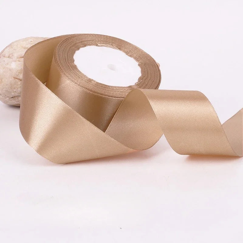 A roll of beige satin ribbon used for gift wrapping and DIY crafts.