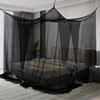 A floor-to-ceiling black mosquito net draped over a bed in a room.