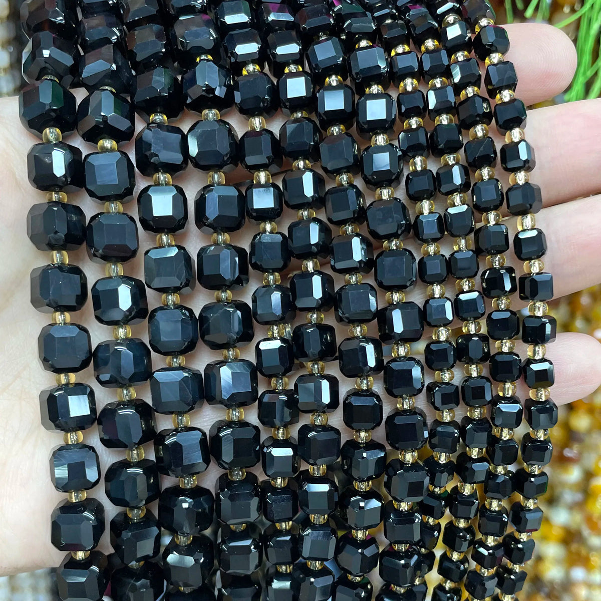 A close-up of black and gold square faceted beads strung together for jewelry making.