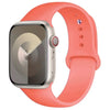 An Apple Watch in a silver case with a bright coral silicone sport band.