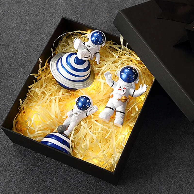 A set of three handcrafted astronaut figurine resin spaceman desk decor figures displayed in a black box with yellow lighting