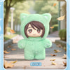 A soft green cat plush doll pendant in a hoodie is displayed outdoors on a wooden path with autumn leaves.