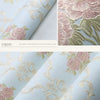 Close-up view of light blue floral wallpaper featuring pink and gold carved leaves and roses.