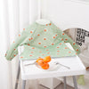 A light green long-sleeve waterproof baby bib with a repeating orange flower pattern displayed on a white table.