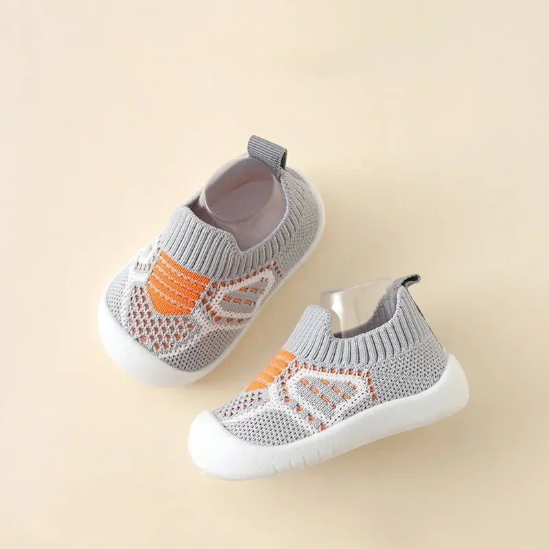 A pair of gray and orange breathable soft-sole baby shoes with a non-slip grip shown from above.