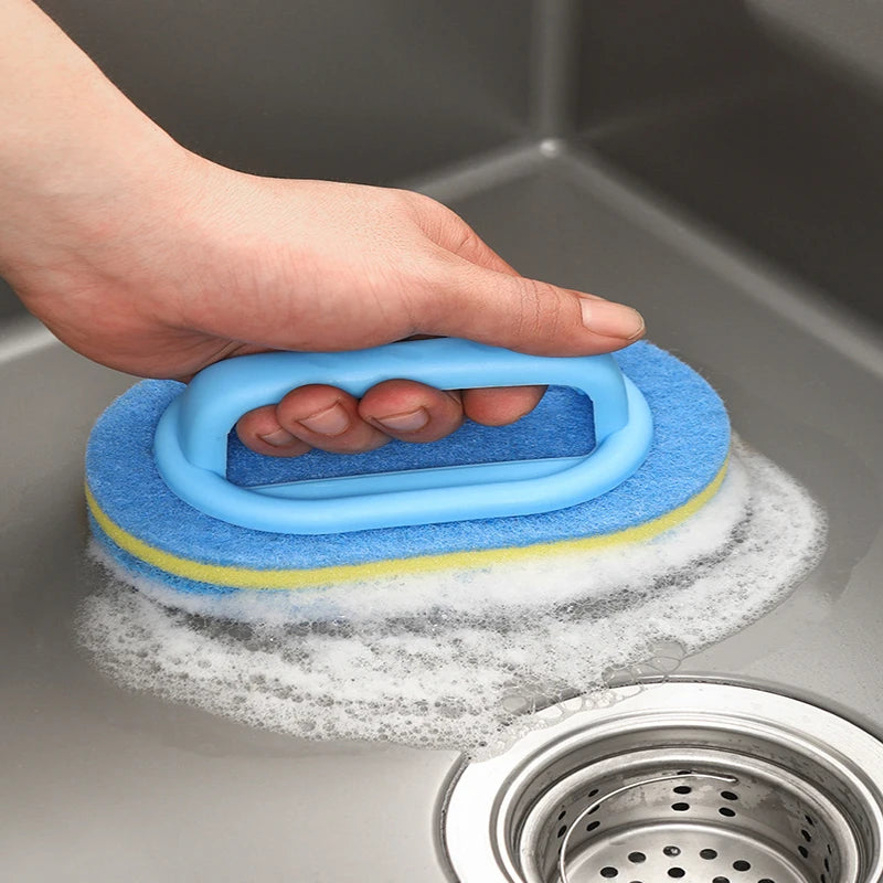 A hand is holding a blue sponge cleaning brush with an ergonomic handle above a metal strainer.