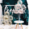 A display of clear plastic balloons in various sizes and shades arranged on a white table against a dark green tropical leaf 