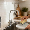 A person is using a touchless automatic soap dispenser to dispense liquid into a sink.