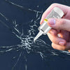 A hand holds a white applicator tip of a windshield glass repair resin kit over cracked dark glass.