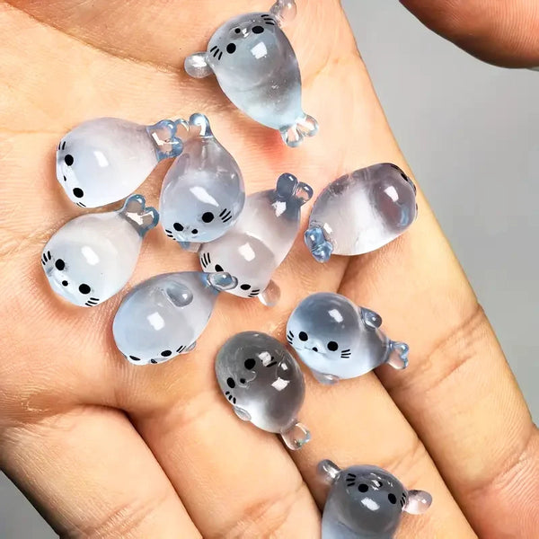 A hand holds several glow-in-the-dark mini seal figurines with light blue and gray translucent bodies.