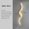A vertical gold LED wall lamp with a curved design mounted on a light gray wall.