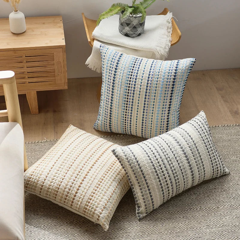 A set of two bohemian linen pillow covers, one blue and white striped, resting on a beige rug.