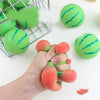 Eine Hand drückt ein Wassermelonen-Stressabbau-Spielzeug mit grünen und roten Farben.