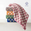 A stack of soft plaid cotton bath towels in various colors including purple, green, orange, and blue.