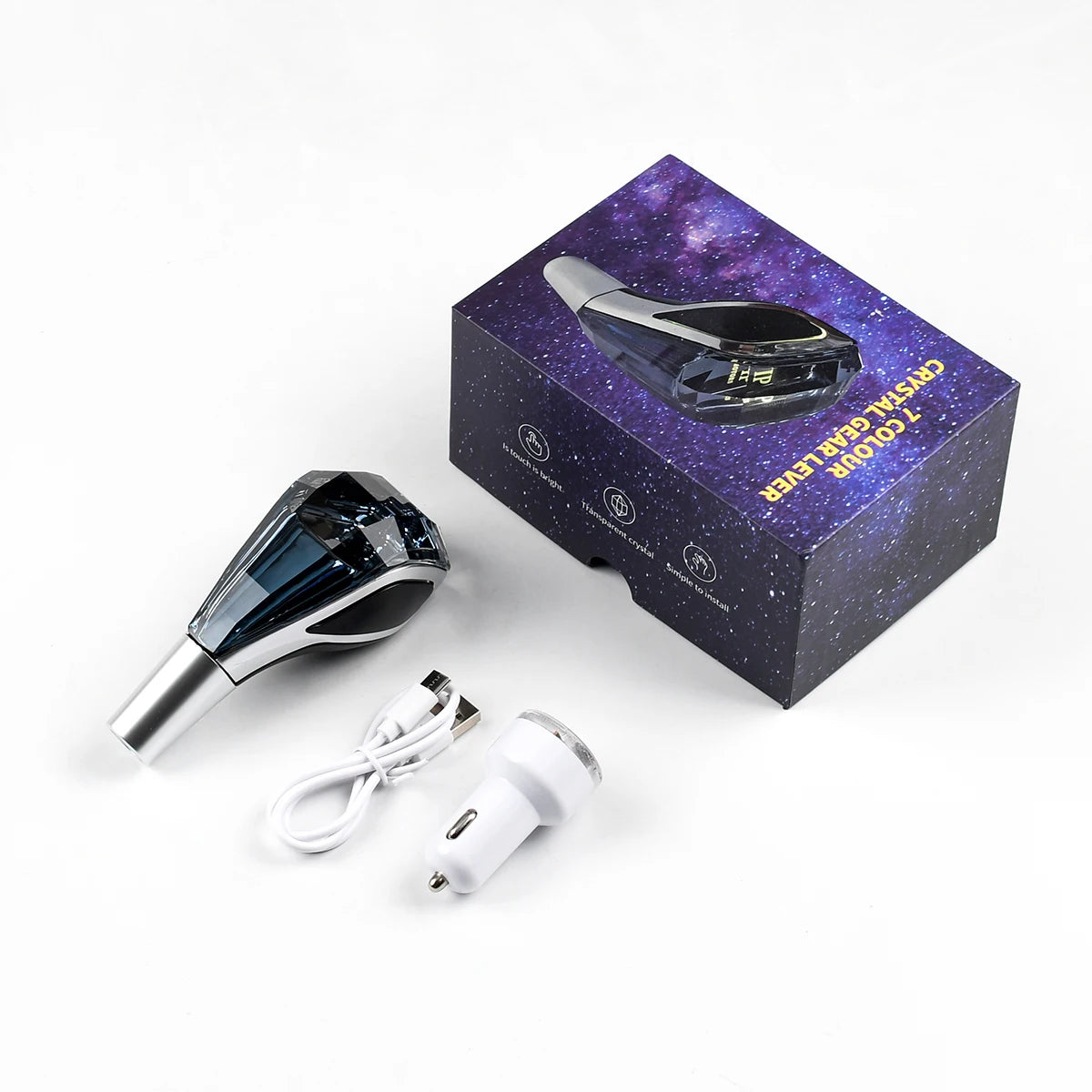 A crystal gear shift knob with a purple galaxy pattern is shown next to its packaging box and electrical cord.